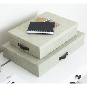 Zwei hellgraue SVERKER Aufbewahrungsboxen A3 von Bigso mit dunklen Griffen werden auf einer weißen Fläche mit einem schwarzen Spiralnotizbuch und zwei braunen Umschlägen gestapelt - perfekt für die Organisation Ihrer Dokumente im Home Office.