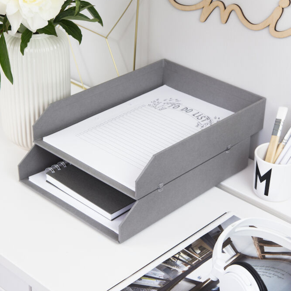 Die HAKAN Dokumentenablage Set 2 Stk. in Grau von Bigso enthält auf der oberen Ablage einen gefütterten To Do List Notizblock und auf der unteren ein geschlossenes Notizbuch, daneben eine Blumenvase, eine Stifttasse und weiße Kopfhörer.