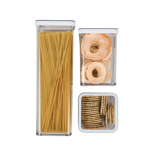 Drei durchsichtige Behälter mit Spaghetti, Apfelringen und Crackern, auf weißem Hintergrund.