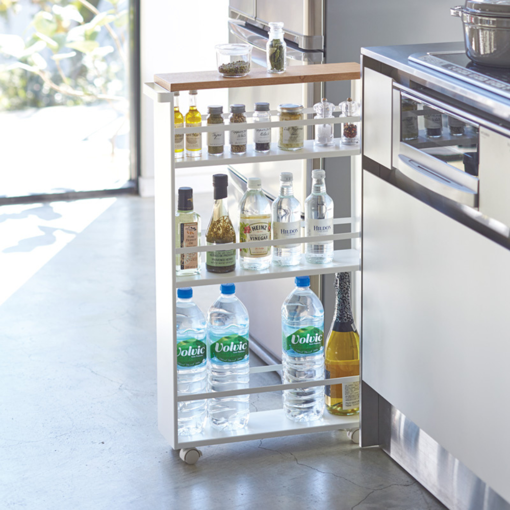 Der YAMAZAKI TOWER Küchenwagen mit Griff in Weiß, mit drei Regalen für Wasser, Öl, Gewürze und mehr, steht platzsparend neben der Küchenzeile am Fenster und sorgt für optimalen Stauraum im Sonnenlicht.