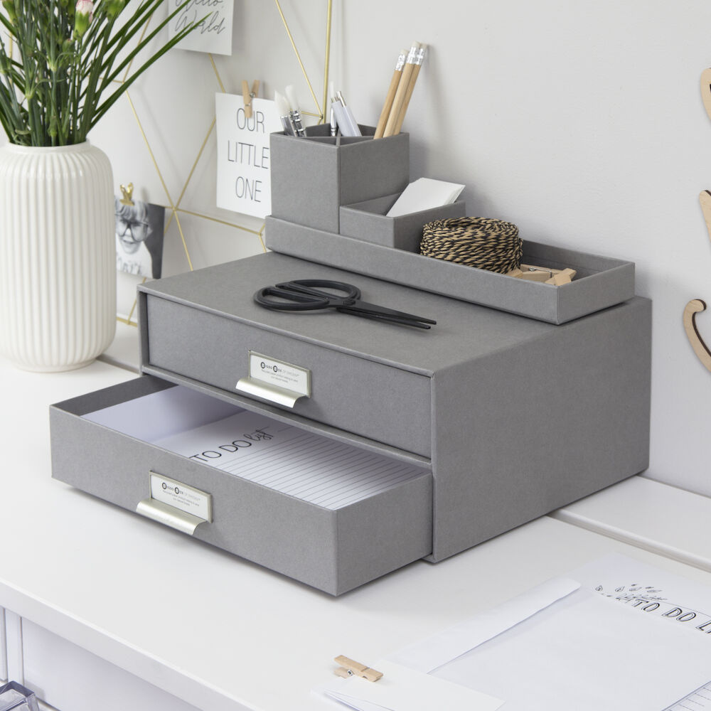 Graue Schubladenbox hält Ordnung auf Schreibtisch mit Schere obenauf.