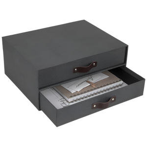 Dunkelgraue Schublade mit Ledergriffen, gefüllt mit Notizbuch und Papieren.