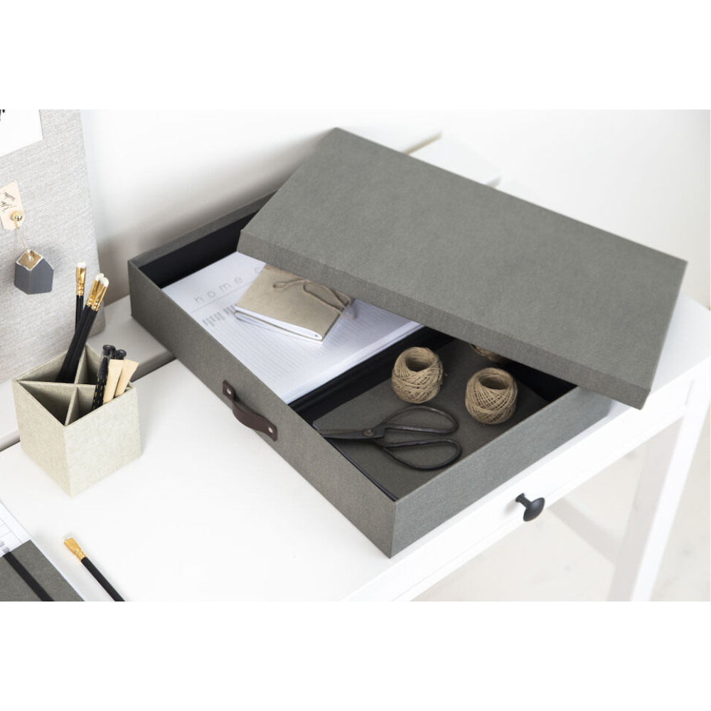 Eine graue Bigso SVERKER Aufbewahrungsbox A3 aus Canvas steht mit halb geöffnetem Deckel auf einem weißen Schreibtisch. Im Inneren: Notizbücher, Schnur und Schere-ideal zur Dokumentenaufbewahrung im organisierten Arbeitsbereich.