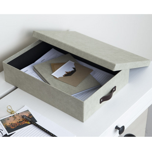 Eine graue Bigso OSKAR Aufbewahrungsbox A4 - Linnen Canvas mit teilweise geöffnetem Deckel steht auf einem weißen Tisch und bewahrt Dokumente und Umschläge auf - ideal für die Organisation von Papierkram in Ihrem Heimbüro.