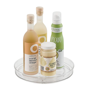 Die iDesign HOME EDIT - Drehteller Lazy Susan KLAR (23x3,5cm) zeigt zwei Flaschen Essig, eine Dose Avocado-Spray und ein Glas Butterschmalz vor einem schlichten weißen Hintergrund.
