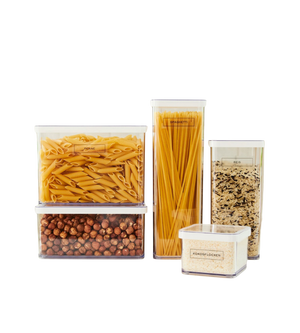 Fünf klare, beschriftete Behälter mit Rotho LOFT Aufkleber - Küchenorganisation organisieren Penne, Spaghetti, Reis, Kichererbsen und kurze Nudeln auf weißem Hintergrund für eine aufgeräumte Küche.