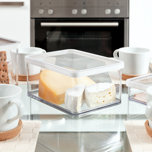 Kunststoffbehälter mit Käse, auf Glastisch mit Tassen in moderner Küche.