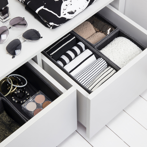 Schubladen mit Kleidung, Accessoires und Brillenetui, daneben Sonnenbrille und Nagellack auf weißer Fläche.