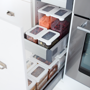 Ein Orthex SmartStore Vorratsdosen KLAR - Weiss Set, jeweils luftdicht verschlossen und gefüllt mit Körnern, Linsen, Bohnen und Nudeln, steht übersichtlich geordnet auf Auszugsböden in einem Küchenschrank neben dem Backofen.