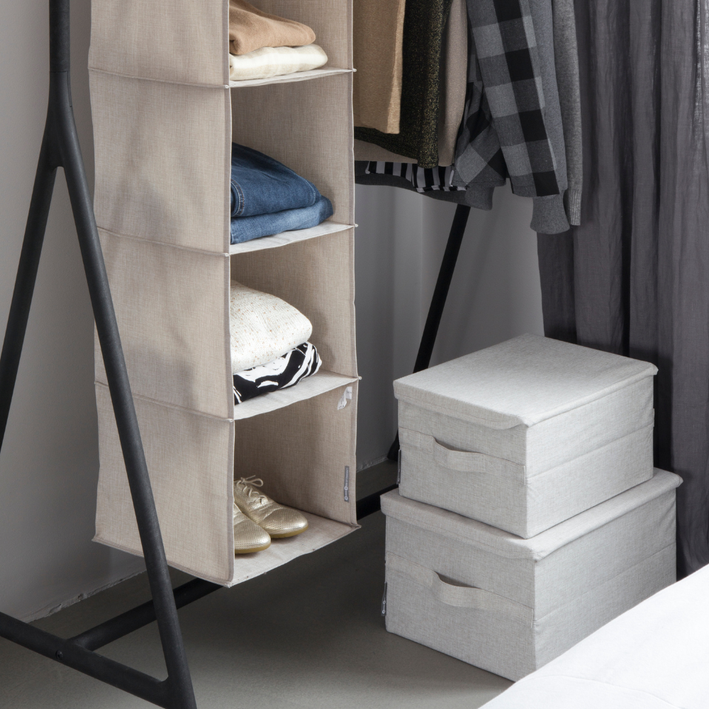 Ein Hängeorganizer aus Stoff mit Kleidung und goldenen Schuhen ist an einem schwarzen Metallkleiderständer befestigt. Zwei beige Bigso SOFT Aufbewahrungsboxen (35x26x19cm) sind auf dem Boden neben dem Organizer gestapelt.