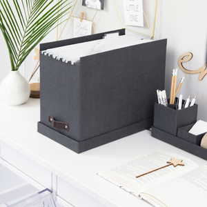 Graue Ablagebox mit Hängeordnern auf einem weißen Schreibtisch, umgeben von Dekorationen.