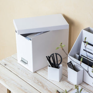 Weiße Aufbewahrungsboxen und Stiftehalter stehen auf einem hellen Holztisch.