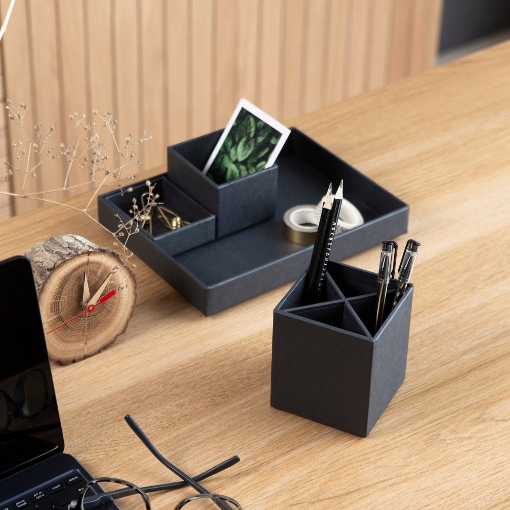 Stiftebecher mit Stiften und Stiftablage auf Holzschreibtisch neben Laptop.